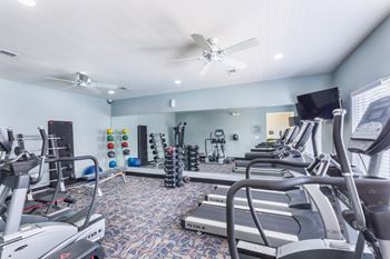 A spacious gym with treadmills, elliptical machines, and a fan.